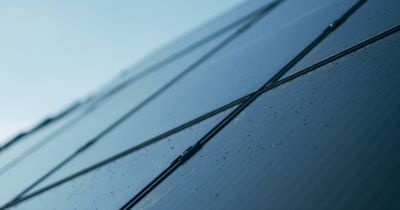 Eine Solaranlage von schräg unten, darauf leichte Regentropfen, ein kleines Stück grauer Himmel oben links